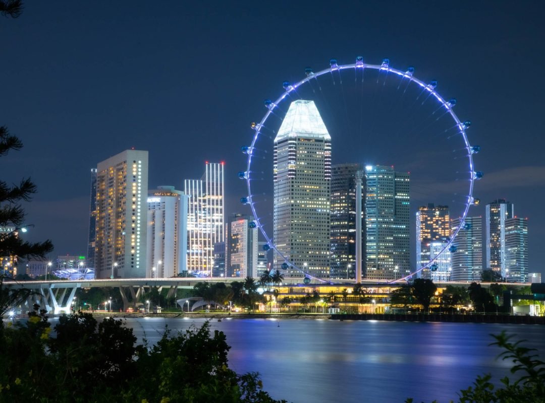 Illuminated Singapore skyline and Ferris wheel reflecting over the water at night.